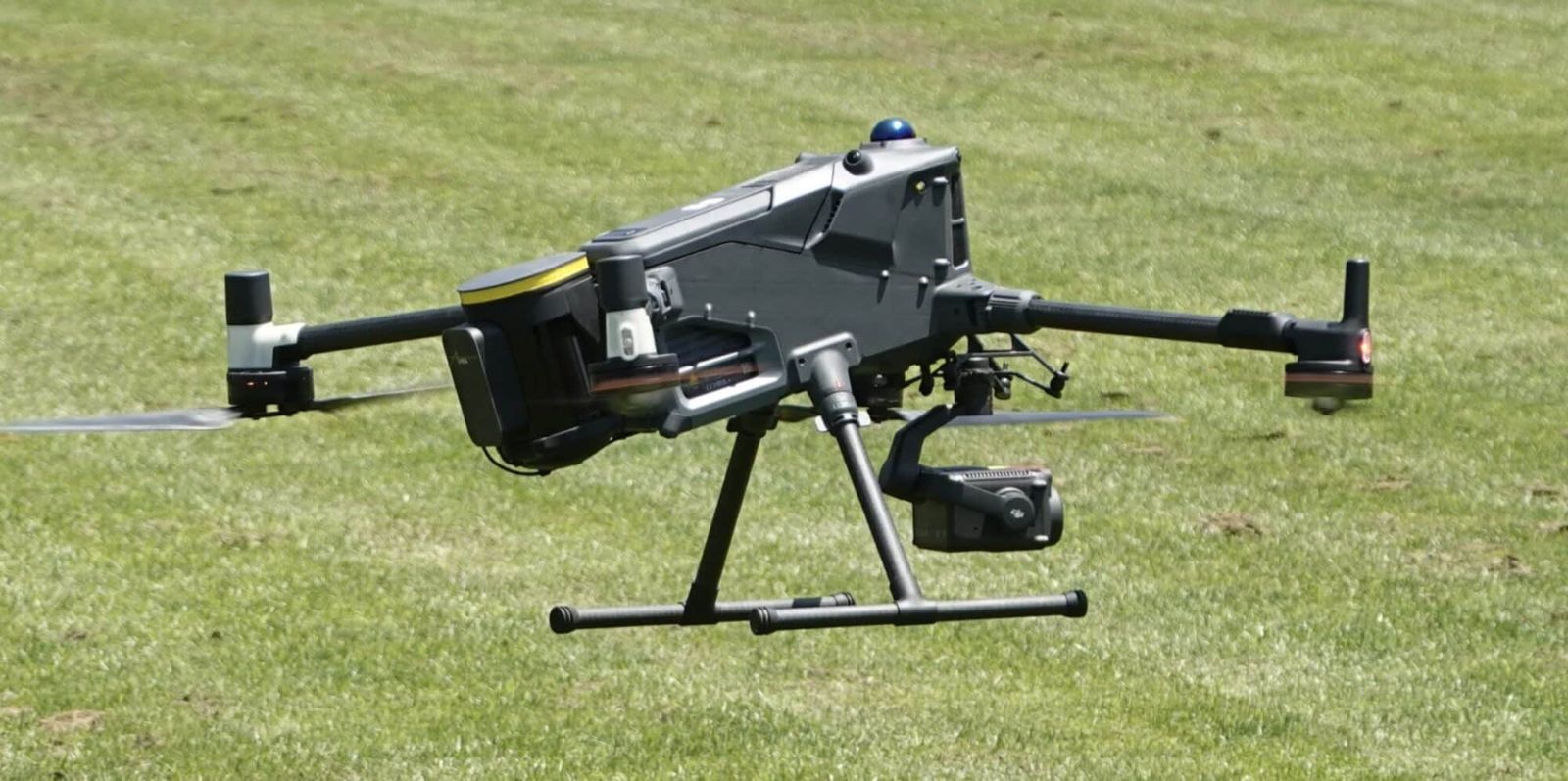 Heavy-lift drone with a camera payload hovering low over a grass field.